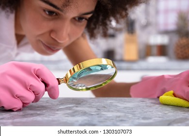 Portrait Of A Young Woman Wearing Pink Gloves Looking At Kitchen Counter With Magnifying Glass
