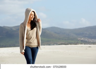 Portrait of a young woman wearing a sweater walking at the beach and looking away at a view - Powered by Shutterstock