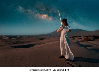 portrait young woman with white dress and lightsaber on a dune in the desert with the milky way in the background