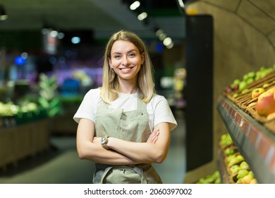 Portrait young woman worker seller in a Vegetable section supermarket standing in arms crossed. greengrocer female looking at camera in fruit shop market Employee in a work apron - Powered by Shutterstock