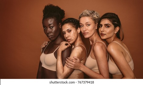 Portrait von jungen Frauen mit unterschiedlichen Hauttypen auf braunem Hintergrund. Verschiedene Gruppen von Frauen, die zusammen stehen und die Kamera anschauen.