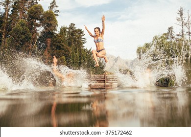 Portrait of young women jumping into a wilderness lake from the jetty. Young girl jumping from a pier at the lake - Powered by Shutterstock