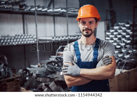 Portrait of a young worker in a hard hat at a large metalworking plant. Shiftman on the warehouse of finished products.