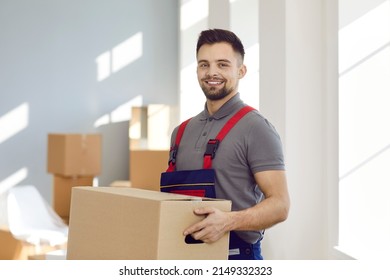 Portrait Of Young Worker From Modern Professional Moving Company Or Express Delivery Service. Happy Handsome Man In Workwear Uniform Standing Inside House, Holding Cardboard Box And Smiling