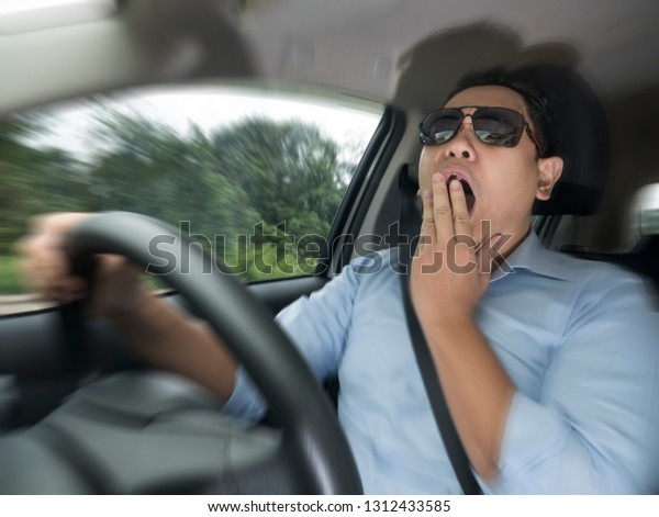 Portrait of yung Asian male driver\
yawning due to sleepy tired while riding a car, danger traffic\
accident insurance concept, zoomed motion blur defocus \
image