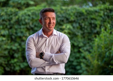 Portraite Of A Handsome Man  In A White Dress Shirt Outside In A Garden.
