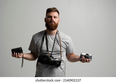 Portraite of professional handsome bearded male photographer with bunch of vintage photo cameras in photo studio, isolated on white background.