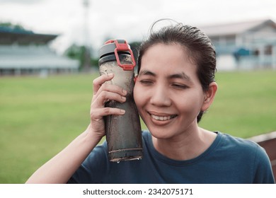 portraits Asian Thai woman holds a cold water bottle against her cheek to reduce heat from exercise.Cheerful and refreshed, heat reduction concept from exercise.