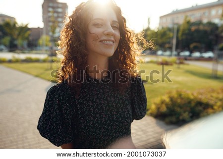 Portraits of a charming red-haired girl with freckles and a pretty face. The girl poses for the camera in the city center. She has a great mood and a sweet smile