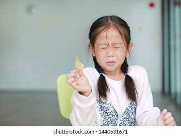 Portraits of cute Asian little girl eating crispy potato chips with face emotion feeling sour.