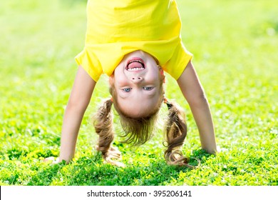 Portraits of happy kid playing upside down outdoors in summertime standing on hands on grass