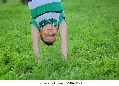 Portraits of happy kids playing upside down outdoors in summer park walking on hands in grass. Adorable little boy hanging upside down having fun outdoors summertime. practice capoeira dance acrobatic