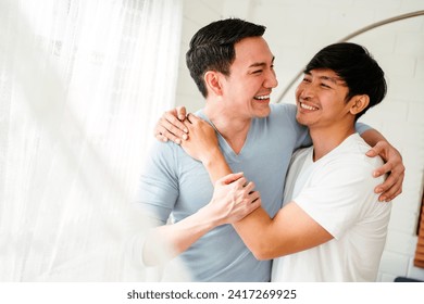 Portraits of happy millennial Asian gay couple hugging and embracing, smiling and laughing in a white curtain window in the living room at LGBT multi-relationship home. An enjoy gay couple concept. - Powered by Shutterstock