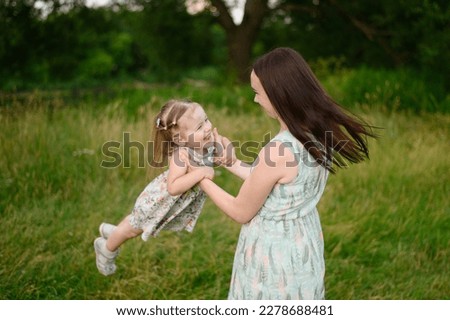 Portraits of a joyful mother and daughter spend time together, smile, have fun, enjoy happy family time and lift her up in the air in the park. Motherhood, lifestyle. Mothers Day