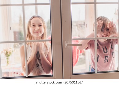 Portraits of little boy and girl, closed on the balcony, on the other side of the glass. Children have fun on the balcony on a sunny summer day. A child behind a glass door. Carefree childhood.