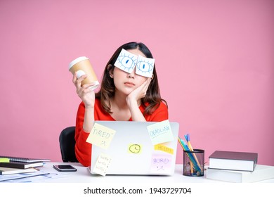 Portraits of overworked Asian women. She was sitting at her desk with stickers covering her eyes and using her laptop on a pastel pink background.