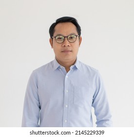 Portrat Close Up Studio Shot Of Asian Happy Middle Aged Chubby Plump Male Model Wearing Optical Eyeglassess With Blue Casual Shirt Standing Smiling Look At Camera In Front Or White Wall Background.