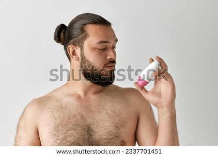 Portreit of handsome man with beard holding jar of cosmetics and looking on it over grey background. Concept of beauty, self care, cosmetic, procedures, health, natural, ad.