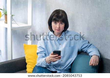 Portreit of plump young woman in strict shirt sits on couch with phone in hands