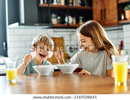 Portret of brother and sister having fun together eating breakfast in kitchen