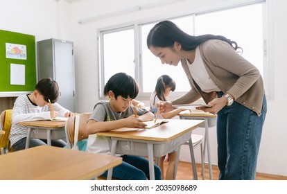 Portriat of  Asian female teacher helping elementary school boy in classroom at school. Education, elementary school, learning concept.