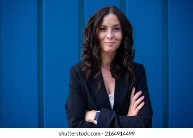 Portriat Of Happy Successful Businesswoman Commuter With Arms Crossed Standing Against Blue Wall Outside In Street.
