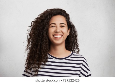 Portriat of pretty curly female wears striped black and whitte t shirt, smiles happily as being glad to meet best friend, who tels her funny jokes or stories. Happiness and facial expressions concept - Powered by Shutterstock