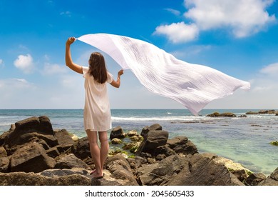 Portriat of young woman with white cloth fabric fluttering in the wind staying on a tropical beach near sea