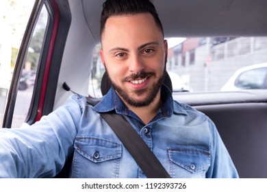 Portrrait Of Handsome Commuter Student Man Smiling And Looking At Camera Using Taxi Cab Service In Back Seat Of Car. Concept Of Commute, Transport Service, Mobility, City Life.