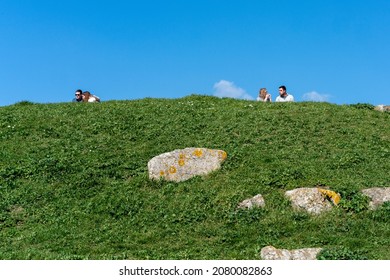 Portsmouth, Hampshire , UK - 24 March 2019: Two Couples Sit Together On Top Of A Grassy Hill Enjoying The Sunshine Under A Clear Blue Sky. There Is A Wide Gap Between Them Maintaining Personal Space.