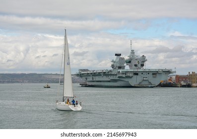 Portsmouth,England, April 14th 2022, Yacht Sailing In Portsmouth Harbour Past HMS Queen Elizabeth, Flagship Of The British Navy.