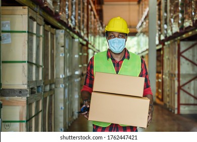 porttrait of african american factory warehosue woker with safety vest and helmet wearing face mask to protect coronavirus covid-19 holding boxes at factory warehouse - Powered by Shutterstock