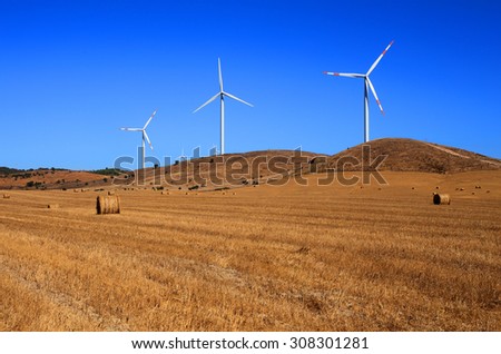 Portugal, Alentejo Region, Wind power turbines in an autumn crop field against a deep blue sky.