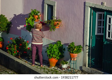 Óbidos, Portugal - December 10, 2018: An Old Woman Watering Plants Outside Her House In The City Of Óbidos, In The Leiria District Of Portugal.