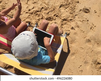 Portugal, Europe - October 09, 2016: Child Using White Apple IPad Air 2 Mobile Tablet On Sunny Beach Outdoors Sea Shore Background