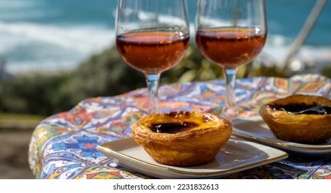 Portugal's traditional food and drink, glasses of porto wine or muscatel de setubal, sweet dessert Pastel de nata egg custard tart pastry served with view on blue Atlantic ocean near Sintra in Lisbon - Shutterstock ID 2231832613