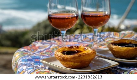 Portugal's traditional food and drink, glasses of porto wine or muscatel de setubal, sweet dessert Pastel de nata egg custard tart pastry served with view on blue Atlantic ocean near Sintra in Lisbon