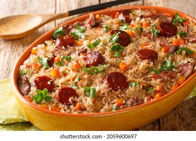 Portugiesischer Entenreis arroz de pato, gekocht mit Rotwein, Zwiebeln, Karotten und Chorizo, Nahaufnahme in der Backform auf dem Holztisch. Horizontal