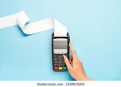 pos terminal with long cash register tape on blue background. female hand presses a pos terminal button. shopping theme