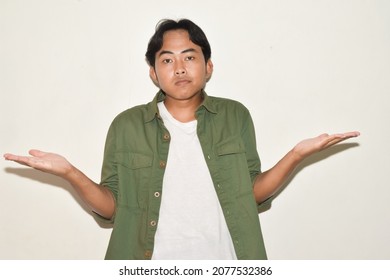 Pose Of Asian Man Shrugging Both Shoulders And Raising Both Hands. Illustrations Of Ignorance, Why Not, Where, And What's Wrong. Portrait Of Indonesian Man On Isolated White Background