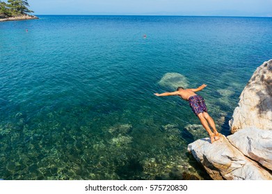 Up pose of man  jumping from massive rocks into calm azure water