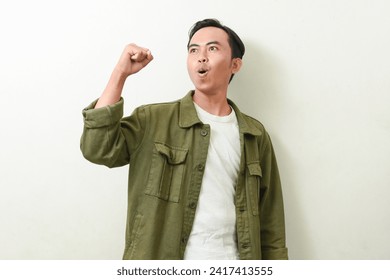 pose of a man screaming, while clenching and raising both hands. illustration of Indonesian men in green jacket being happy and excited. stock photos about enthusiasm, optimism, win, spirit, future