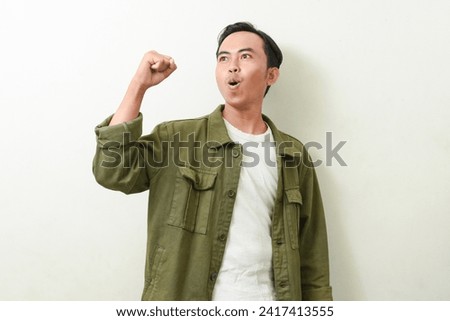 pose of a man screaming, while clenching and raising both hands. illustration of Indonesian men in green jacket being happy and excited. stock photos about enthusiasm, optimism, win, spirit, future
