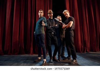 Posing for a camera. Group of actors in dark colored clothes on rehearsal in the theater.