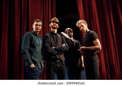 Posing for a camera. Group of actors in dark colored clothes on rehearsal in the theater.