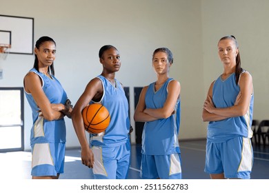 Posing confidently in gym, female basketball team holding basketball. Sports, teamwork, exercise, strength, empowerment, competitiveness - Powered by Shutterstock