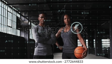 Posing fit pair wearing compression top and sleeveless at warehouse gym, holding basketball and HUD. Duo, athletes, training, athleticwear, industrial, daylight, concrete