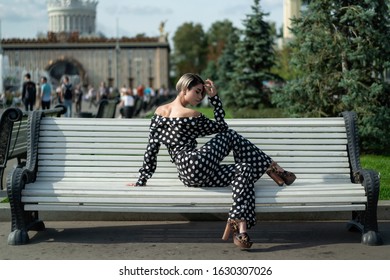 posing on a park bench. beautiful European model in a black trouser suit with white spots, pants and a shirt, high heel. Short haircut, bright makeup, long legs. female lessons posing - Powered by Shutterstock