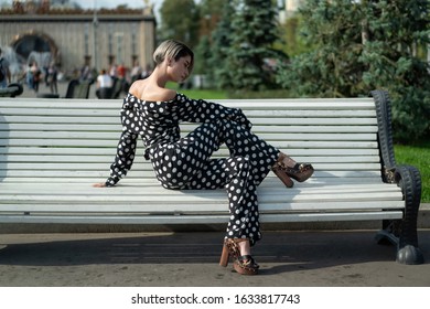 posing on a park bench. beautiful European model in a black trouser suit with white spots, pants and a shirt, high heel. Short haircut, bright makeup, long legs. female lessons posing - Powered by Shutterstock