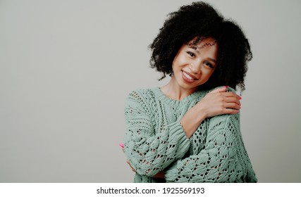 Posing in a photo studio smiling. The woman is dressed in a modern warm mint-colored sweater. Happy Portrait of a beautiful Young Afro appearance and curly hair. copy space.